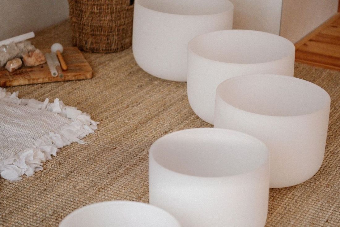 Multiple frosted crystal singing bowls arranged on a natural jute rug with crystals and mallets at Prana Blessings