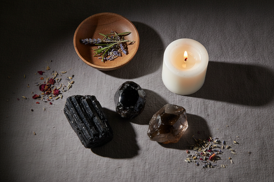Black Tourmaline, Obsidian, and Smoky Quartz crystals arranged in a moody atmospheric flat lay with a lit white pillar candle and earthy props