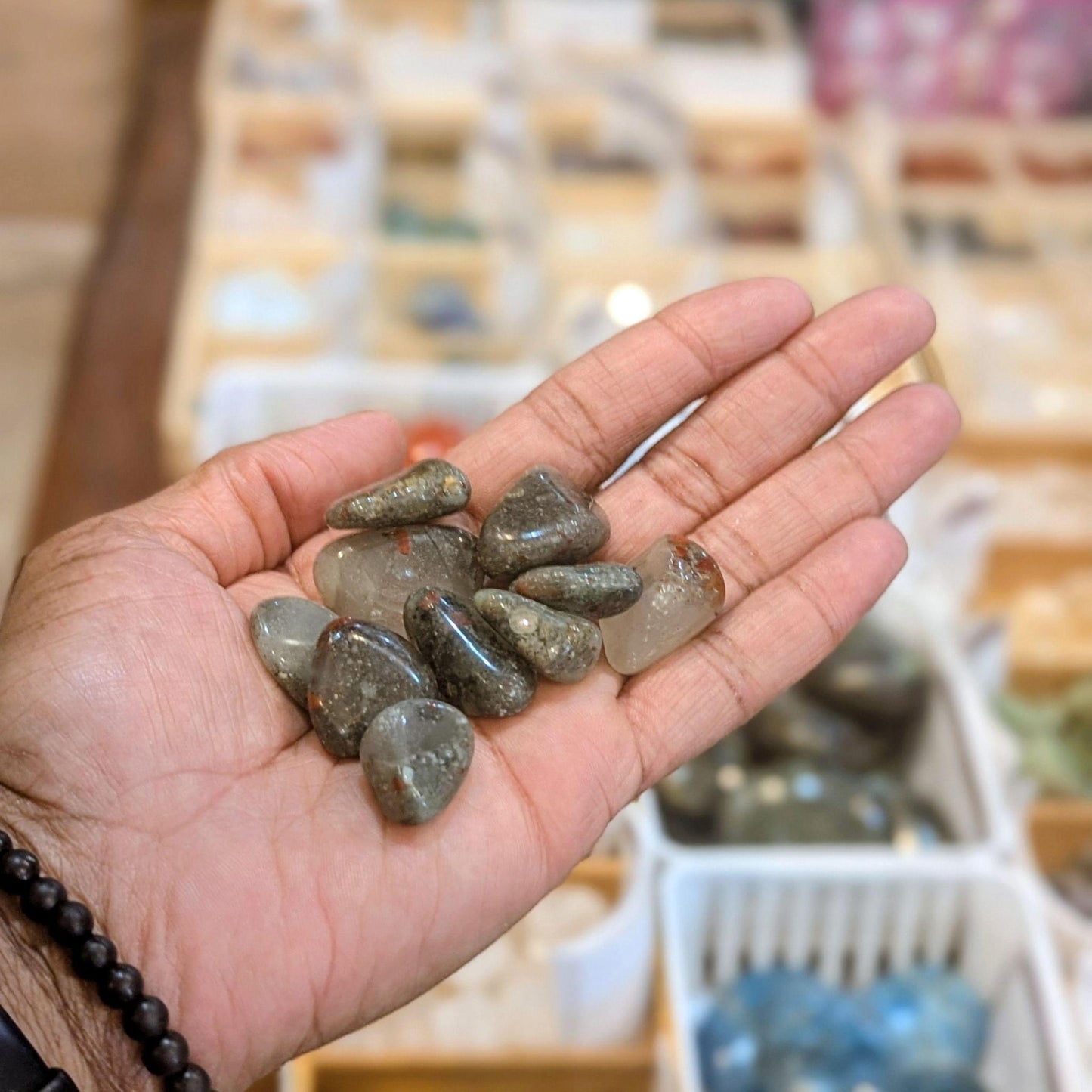 Polished African Bloodstone tumbled stones held in an open hand, showing their size and mottled dark gray, black, and red variation.