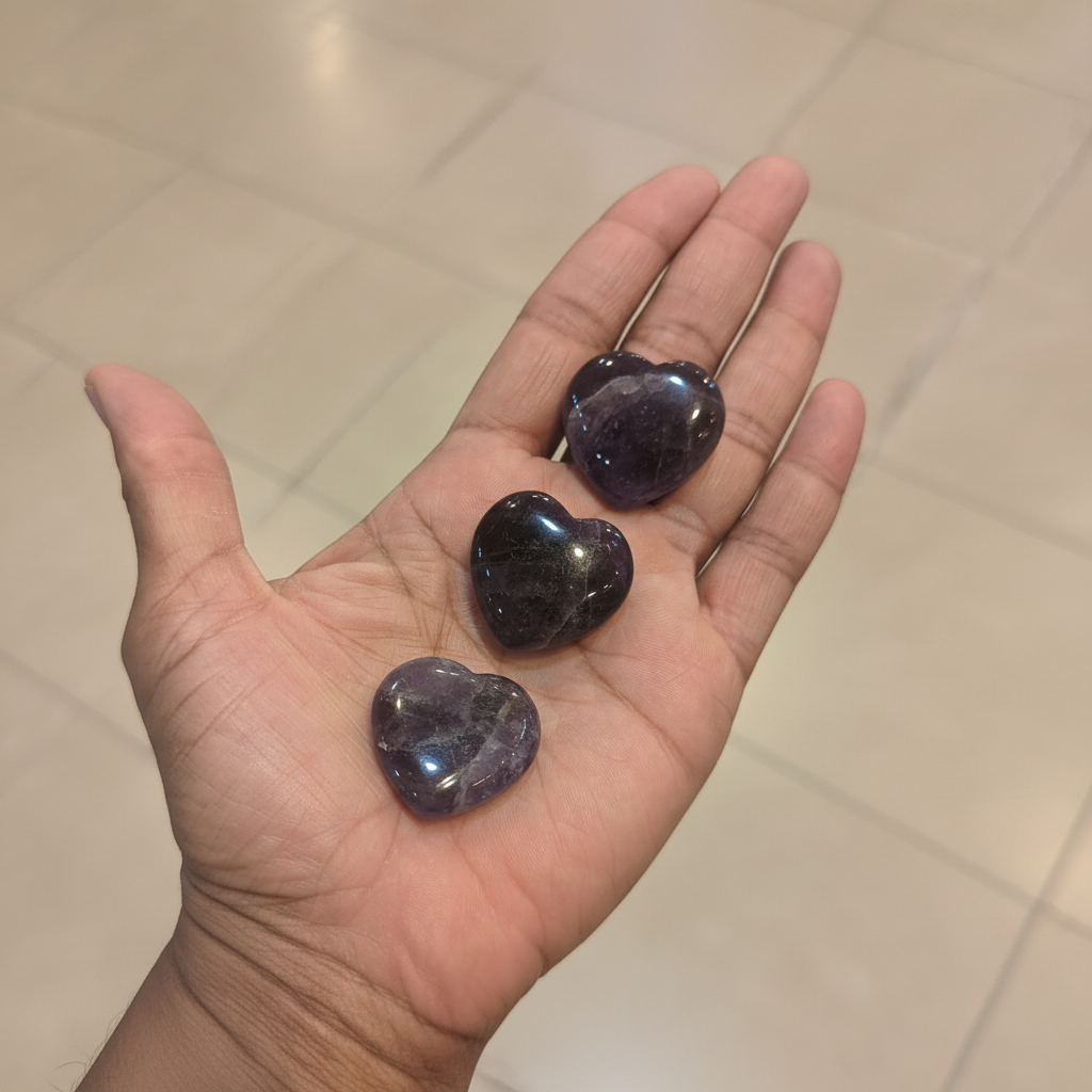 Small polished purple amethyst heart crystals held in an open hand, showing their size and natural color variation.