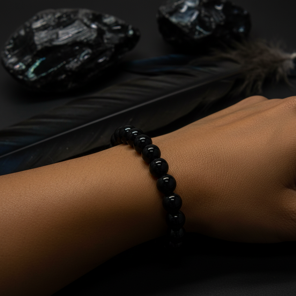 Black Obsidian 8mm bracelet worn on wrist in dramatic moody lighting with raw obsidian stones in background — Prana Blessings