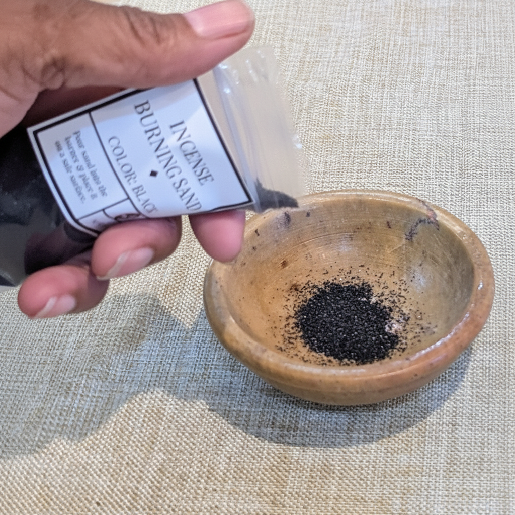 Black sand being poured into a heat-safe incense burner