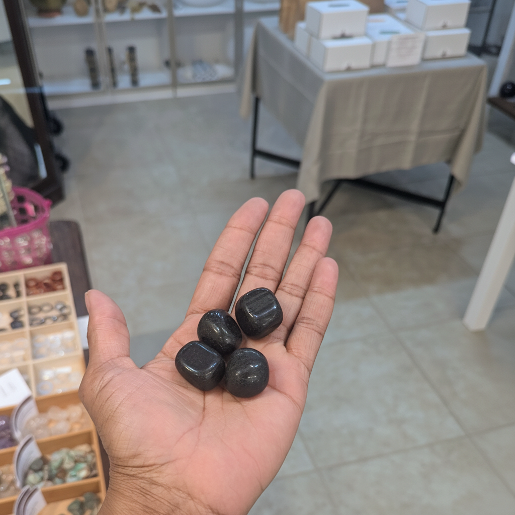 Polished black tourmaline tumbled stones held in an open hand, showing their size and natural variation.