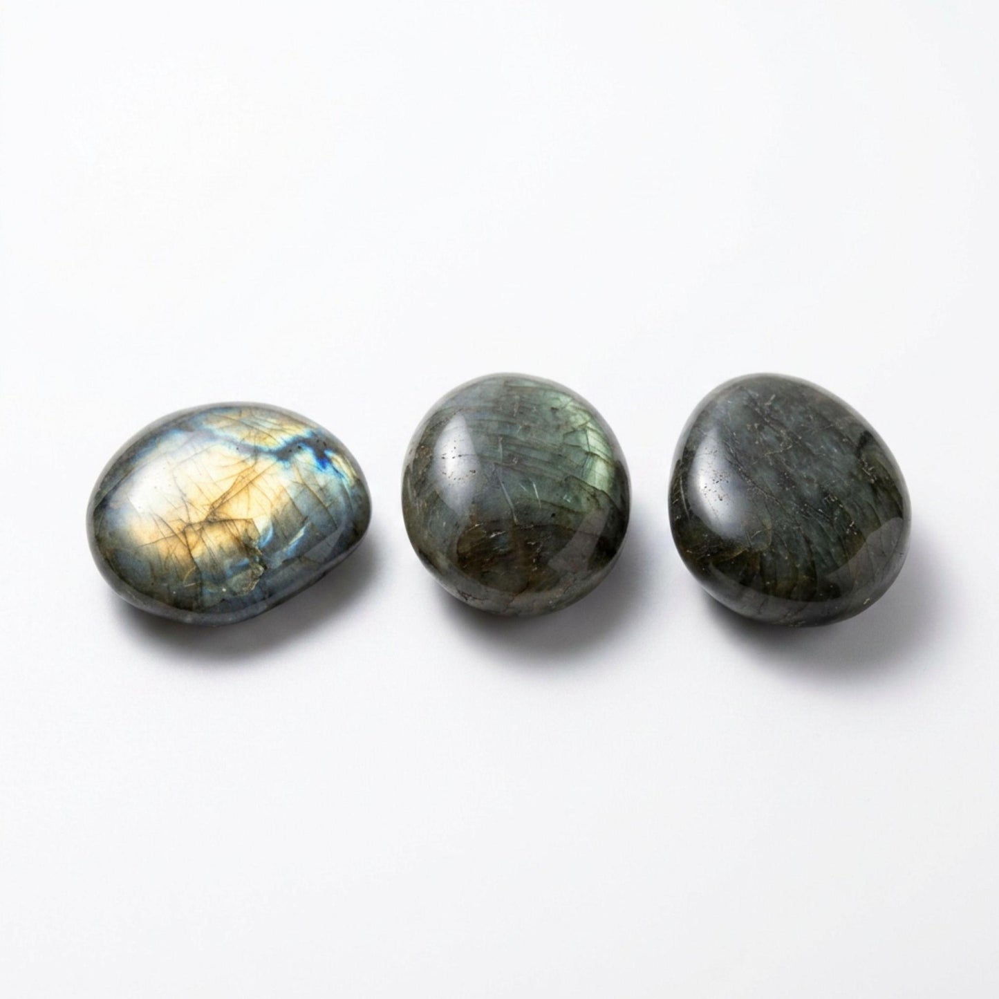 Three polished labradorite stones in oval shapes, arranged horizontally on a clean white background. The stones display natural iridescent flashes of gold, blue, and green.