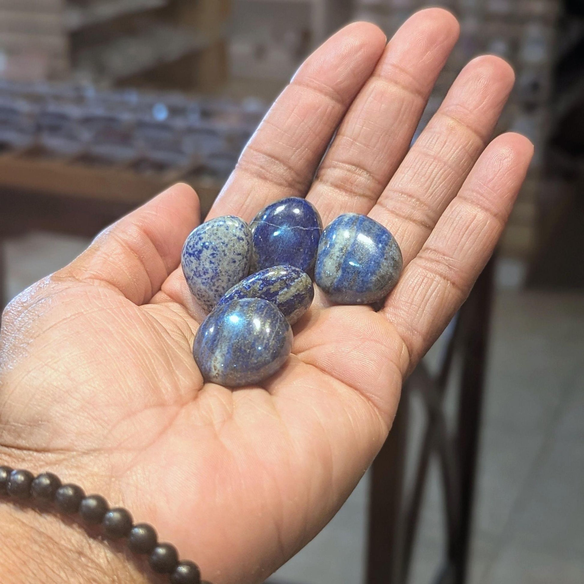 Polished deep blue Lapis Lazuli tumbled stones held in an open hand, showing gold-colored flecks, size, and natural variation.