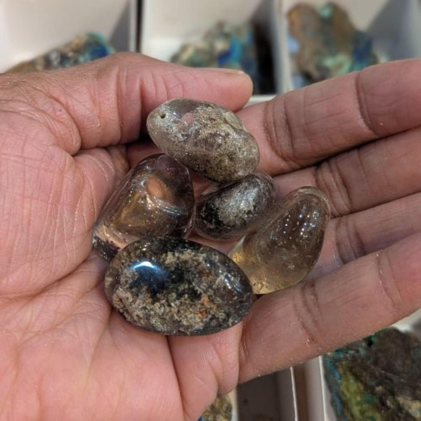 Polished Garden Quartz tumbled stones held in an open hand, showing their clear, smoky, and earthy natural inclusions.