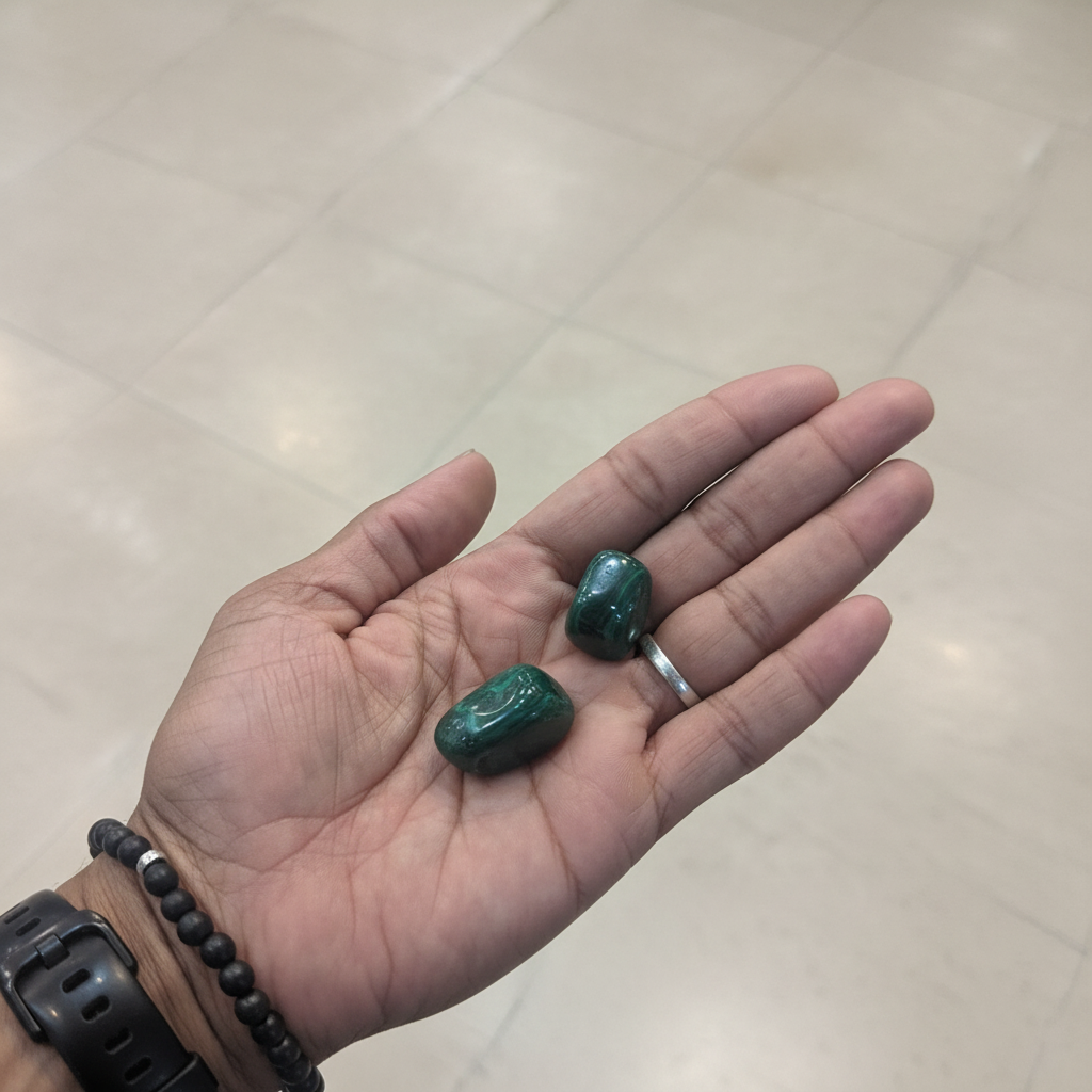 Polished green malachite tumbled stones held in an open hand, showing natural banding, size, and variation.