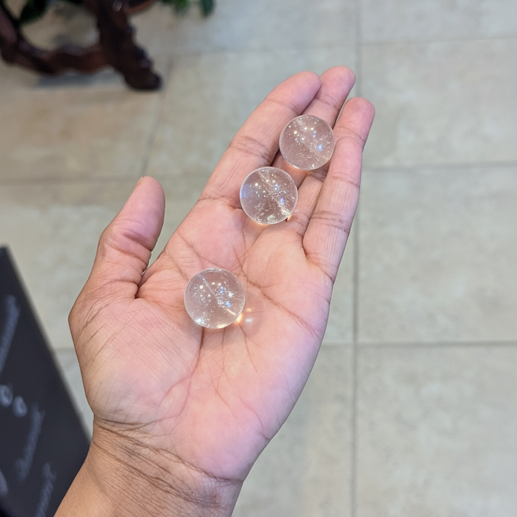 Mini polished Clear Quartz spheres held in hand to show approximate scale