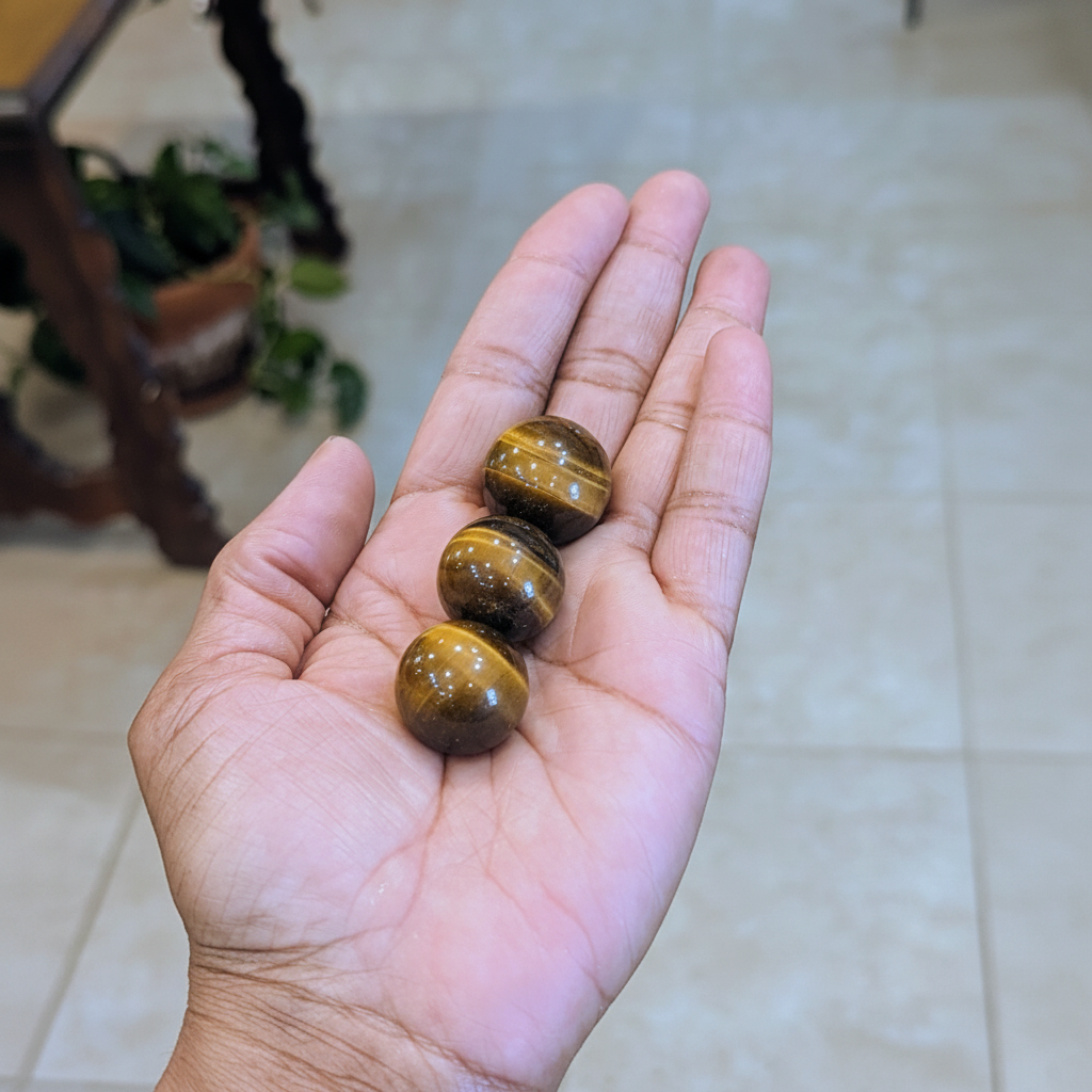 Mini polished golden-brown Tiger’s Eye spheres held in hand to show approximate scale