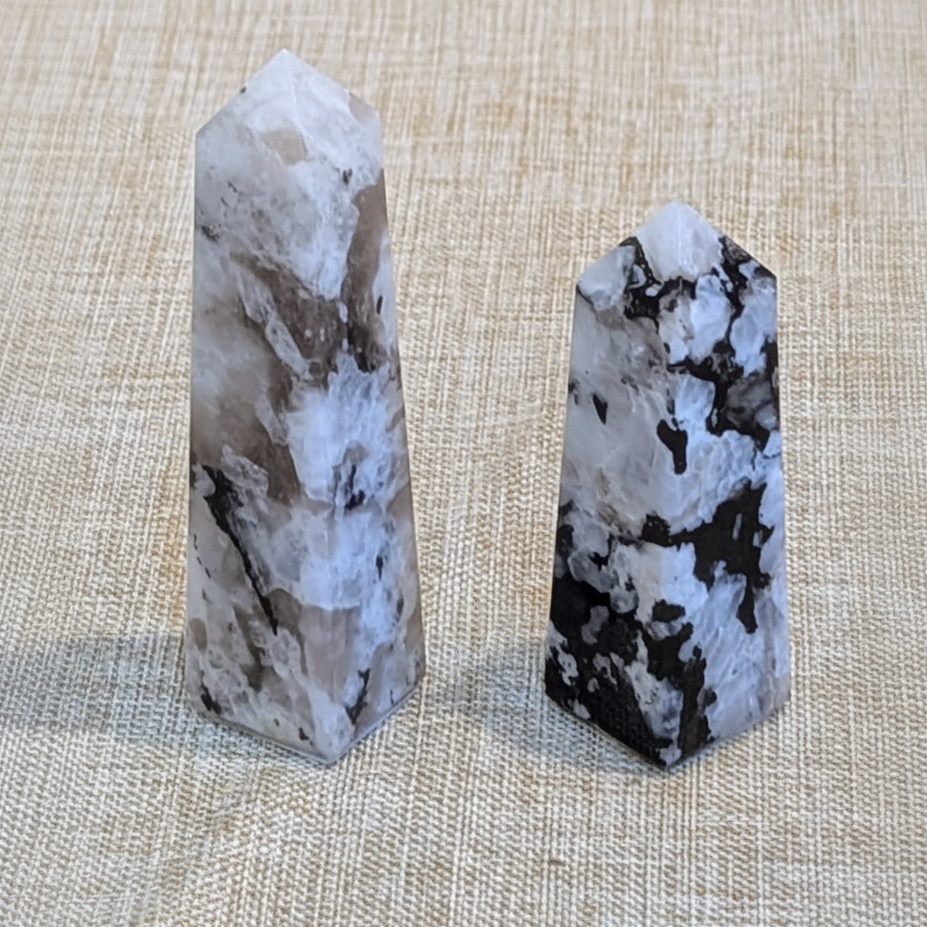 Polished 4-inch Rainbow Moonstone obelisk with natural dark inclusions held in hand to show approximate scale