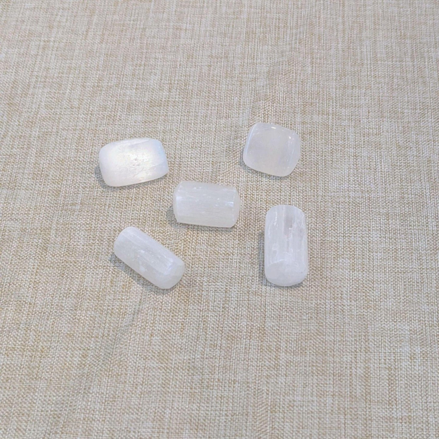 Five small white, selenite polished stones with rounded rectangular shapes arranged on a beige linen fabric background.