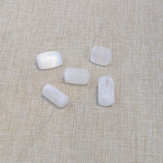 Five small white, selenite polished stones with rounded rectangular shapes arranged on a beige linen fabric background.